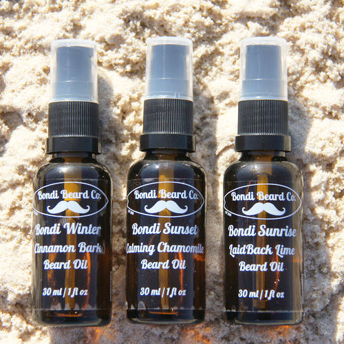 Image of Bondi Beard Co. Bondi Triple Beard Oil collection. Three brown spray bottles laying on sand in the sun.