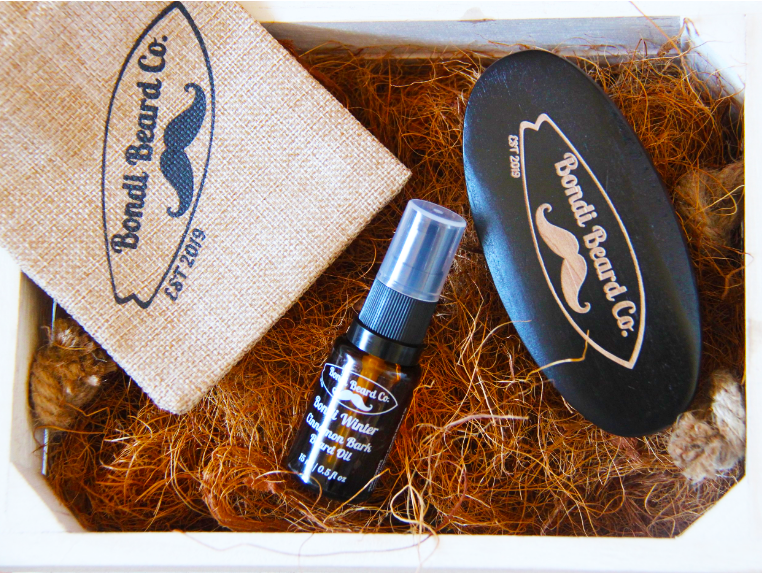 Image of Bondi Beard Co. Cinnamon Bark Beard Oil, Bondi Beard Co. Boar Bristle Brush, branded hessian pouch, and sitting in box with copper packing fibres.