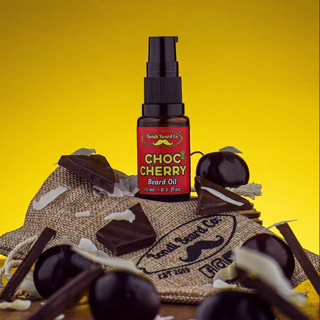 Image of Bondi Beard Co. Choc Cherry Beard Oil in brown spray bottle sitting on branded hessian bag and decorated with dark cherries and dark chocolate shards.