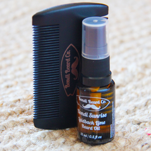 Image of small black atomising bottle of beard oil with a black two-sided comb, both with Bondi Beard Co. branding and sitting on a fibrous mat