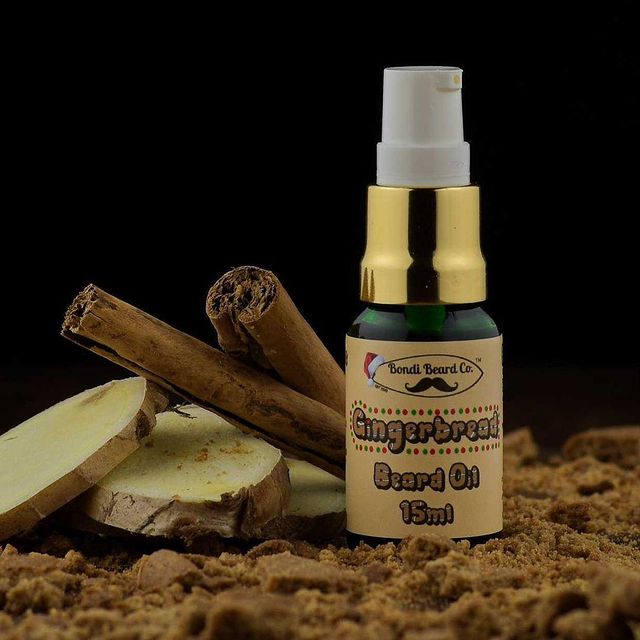 Image of Bondi Beard Co. Gingerbread Beard Oil spray bottle sitting on gingerbread crumbs, and positioned in front of cinnamon sticks and pieces of fresh ginger.